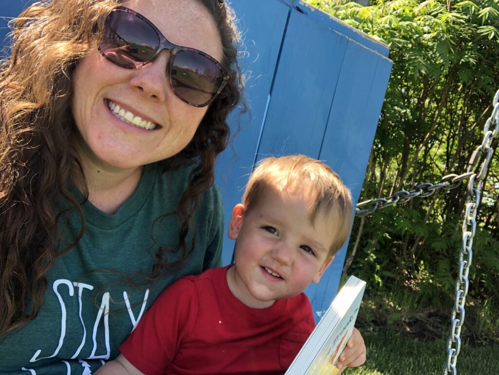 Mom with sunglasses and 1 year old reading a book on a blue swing