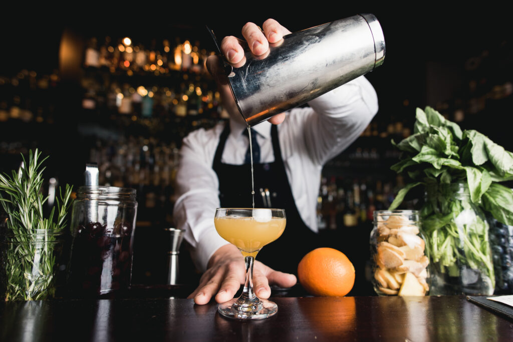 bartender pouring orange drink, orange and herbs in background. Adobe Stock photo
