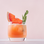 orange cocktail with a slice of fruit and herb in it