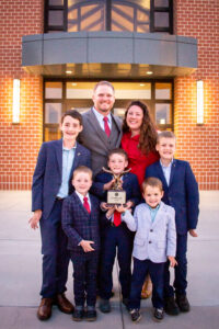 dad, mom, and 5 boys stand in front of a brick church, wearing suits and smiling